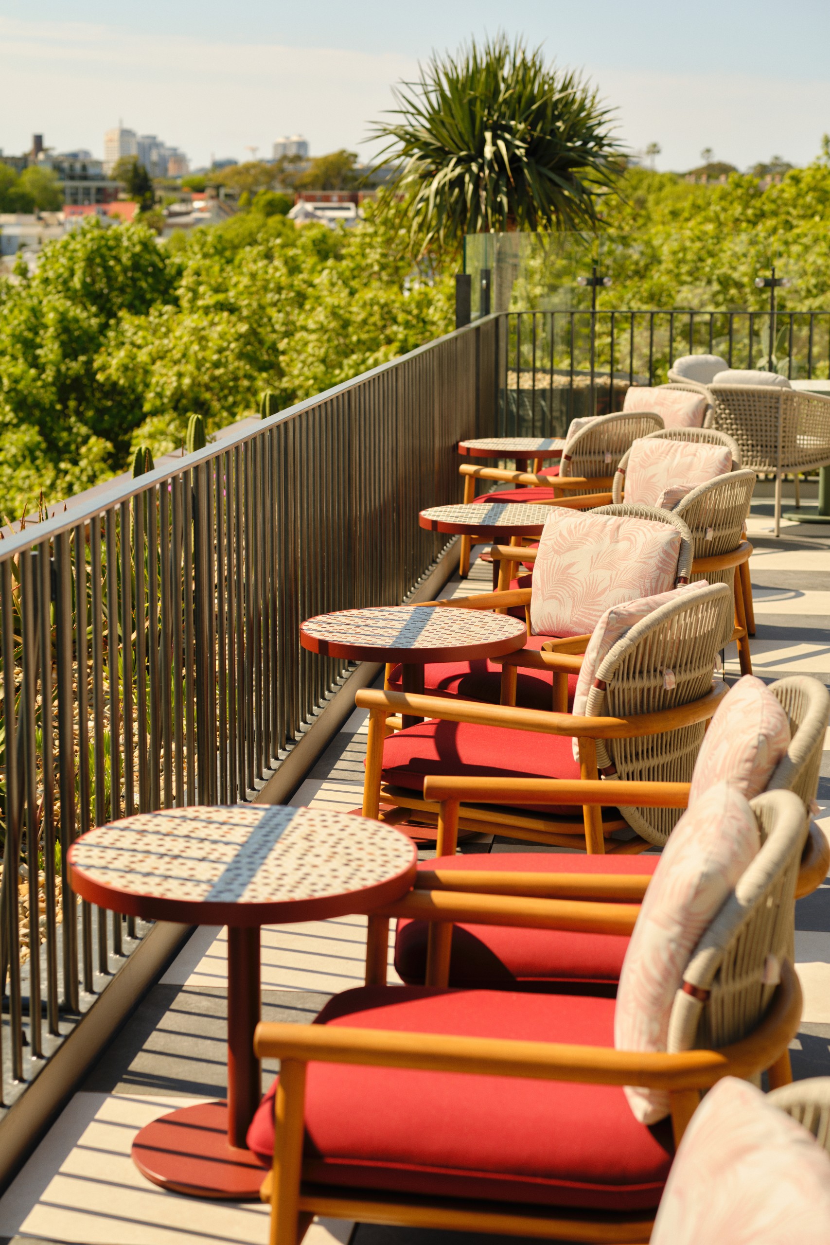 A sunlit balcony featuring stylish wicker chairs with floral cushions and circular tables, overlooking a lush green landscape.
